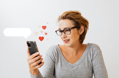 Une femme consulte son smartphone, entourée de symboles évoquant les rencontres en ligne. Une illustration du choix permanent proposé par les applications de rencontre et de notre tendance à comparer les profils plutôt qu'à prendre le temps de découvrir une personne.